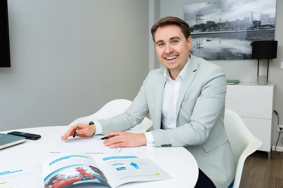 Steffen Lindig sitzend mit Dokumenten, lächelnd.